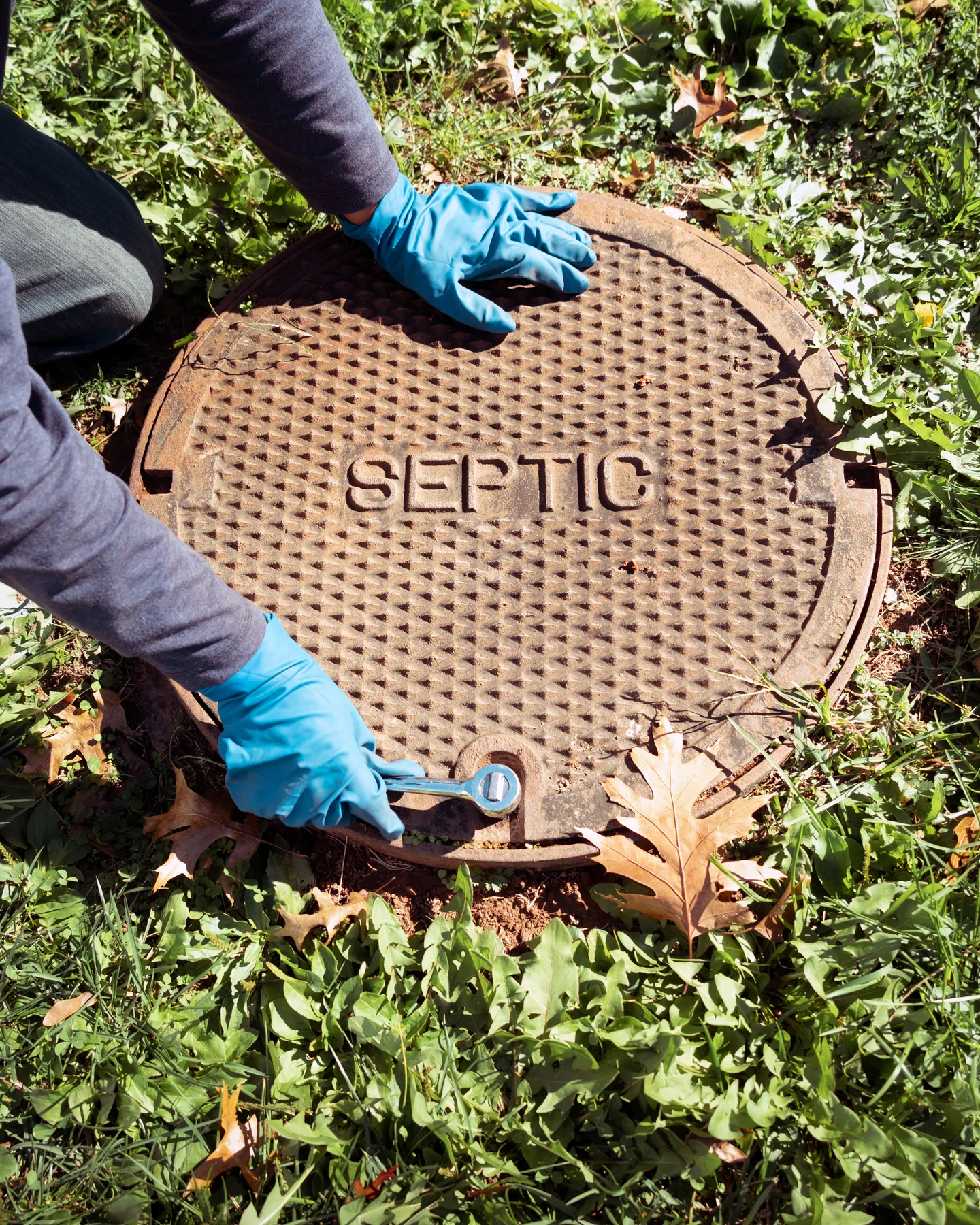 Technician in gloves opening a cast iron septic lid in the grass
